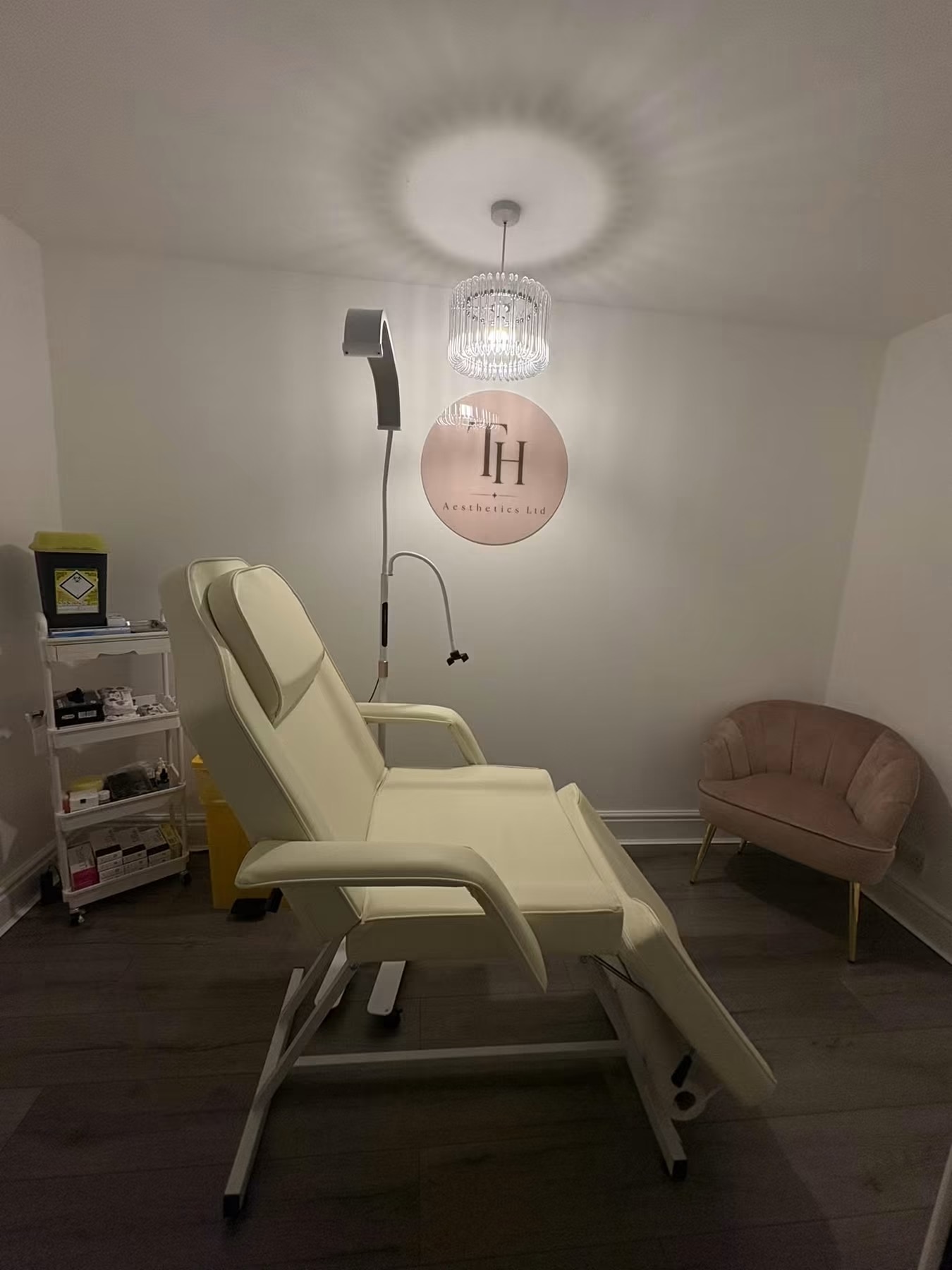 Actual TH Aesthetics treatment room with cream treatment chair, blush seating and chandelier